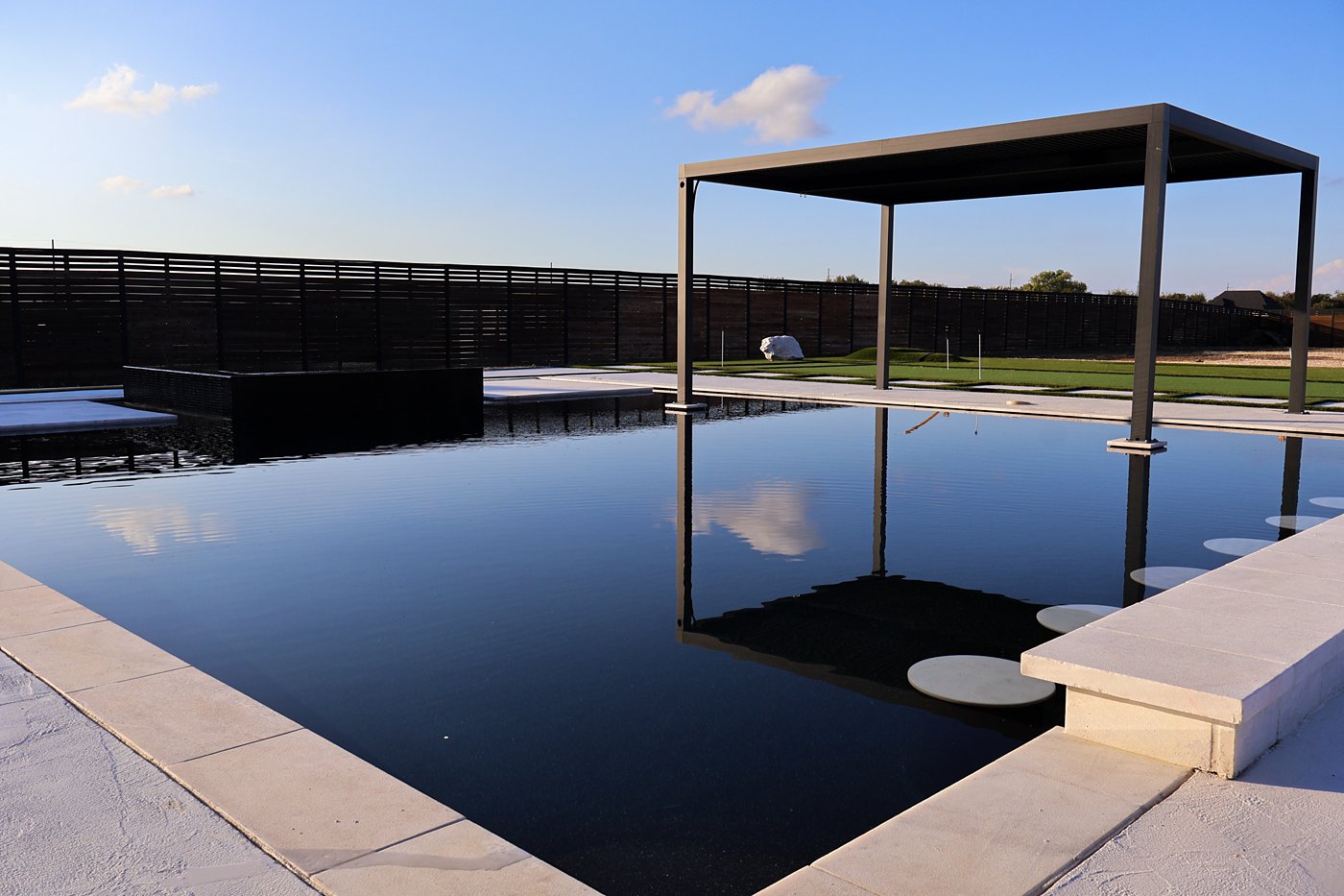 Black mirror-finish pool with a modern pergola and stepping pads in the water