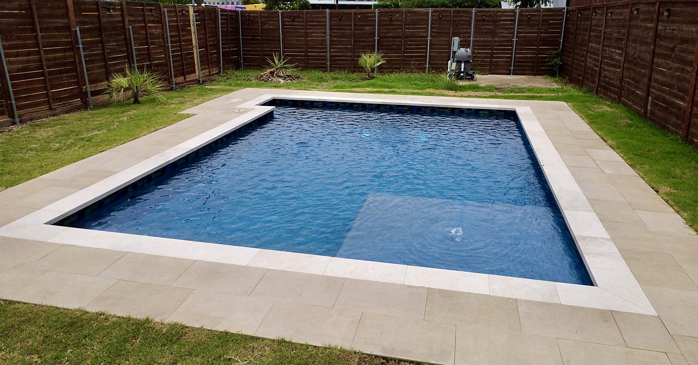 Rectangular pool with a sun shelf, glass waterline tile and stone deck