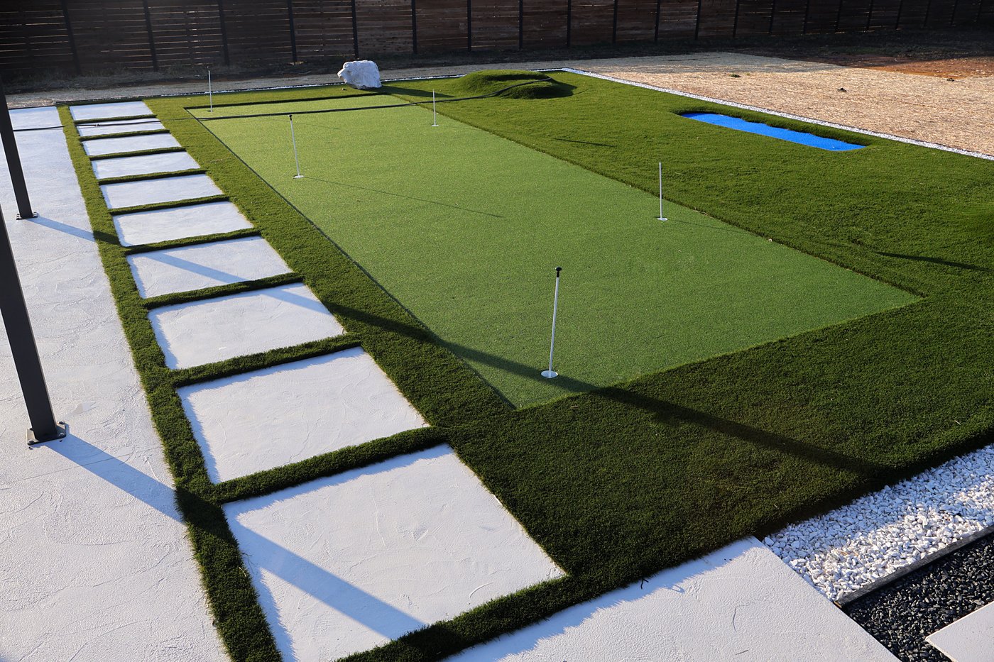 Turf putting green framed by large pavers and river rock