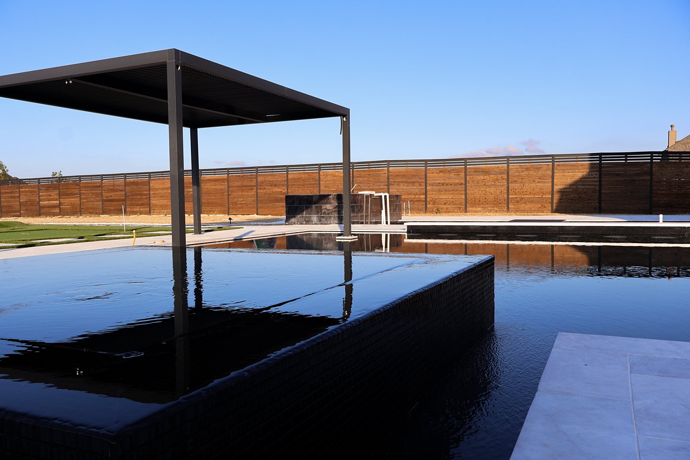 Raised black-tile spa beside a mirror-finish pool under a pergola