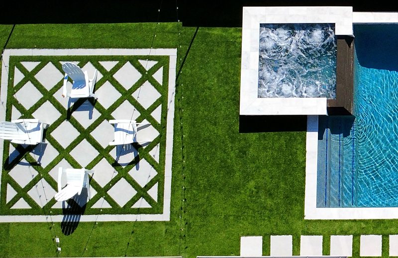 Raised spa with spillway next to a diamond-pattern turf and paver lounge